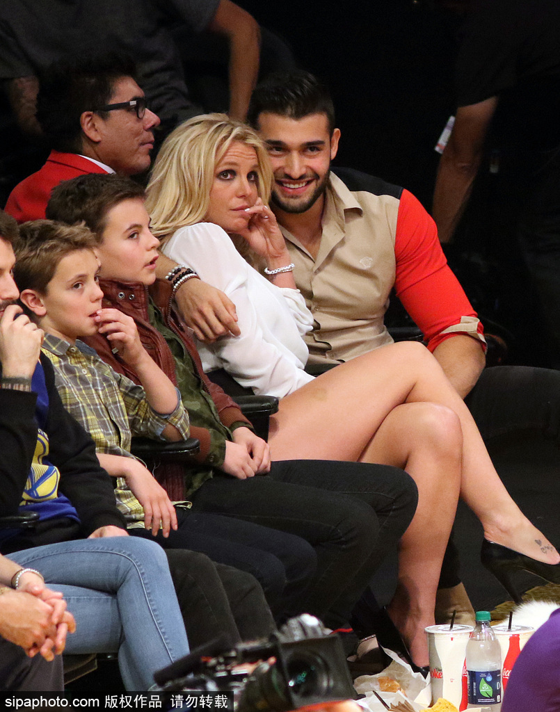 当地时间2017年11月29日，美国洛杉矶斯台普斯中心，“小甜甜”布兰妮（Britney Spears）携男友Sam Asghari与孩子一道观战湖人队比赛，亲密交谈其乐融融。